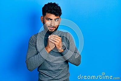 Arab man with beard wearing turtleneck sweater laughing nervous and excited with hands on chin looking to the side Stock Photo