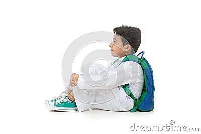 Arab school boy sitting on ground with a smile on his face, wearing white traditional Saudi Thobe, back pack and sneakers, raising Stock Photo