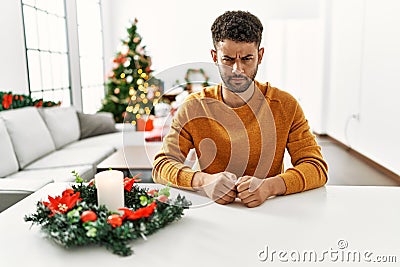 Arab young man sitting on the table by christmas tree skeptic and nervous, frowning upset because of problem Stock Photo