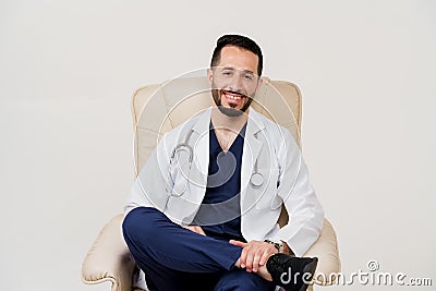 Arabian doctor surgeon in medical robe with phonendoscope seats and smile in armchair in studio on white blanked Stock Photo
