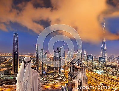 Arabian man watching night cityscape of Dubai with modern futuristic architecture in United Arab Emirates Stock Photo