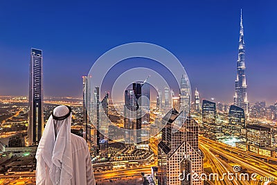 Arabian man watching night cityscape of Dubai with modern futuristic architecture in United Arab Emirates Stock Photo