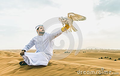 Arabic man with traditional emirates clothes walking in the desert with his falcon bird Stock Photo