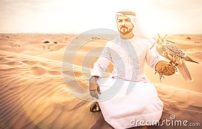 Arabic man with traditional emirates clothes walking in the desert with his falcon bird Stock Photo