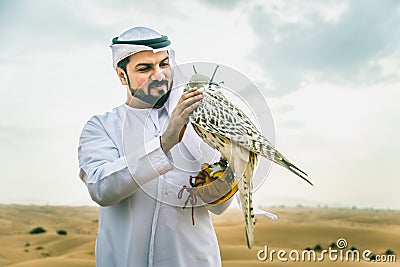 Arabic man with traditional emirates clothes walking in the desert with his falcon bird Stock Photo