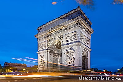 Arc de Triomphe at dusk in Paris in France with traffic of cars light trails and yellow leafs moved by the wind Stock Photo