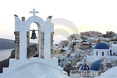 Arch with a bell, white houses and church with blue domes in Oia or Ia at golden sunset, island Santorini, Greece. - Immagine Stock Photo