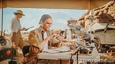 Archaeological Digging Site: Great Male Archaeologist Doing Research, Uses Smartphone to Share Stock Photo