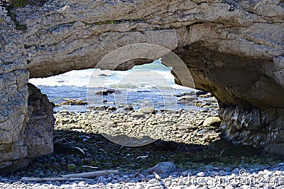 The Arches rock formation framing boulder filled beach with crashing waves Stock Photo