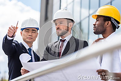 Architects in hardhats working with blueprint outside modern building Stock Photo