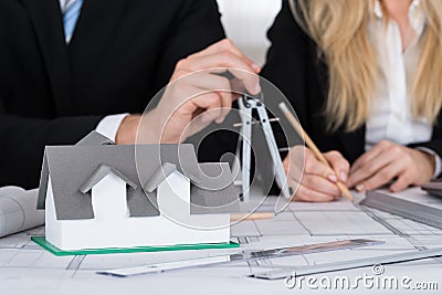 Architects Working On Blueprint With House Model On Desk Stock Photo