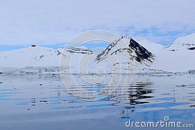 Arctic landscape with reflections in the water of snowy mountains and blue sky, Svalbard archipelago, Norway Stock Photo