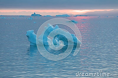 Arctic nature landscape with icebergs in Greenland icefjord with midnight sun sunset / sunrise in the horizon. Early morning Stock Photo