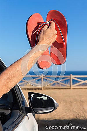 Arm in car showing bath slippers at sea Stock Photo