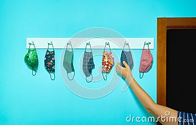 Arm of a person picking up a hygienic mask. Anti-Covid-19 masks hanging from a coat rack. New normal concept Stock Photo