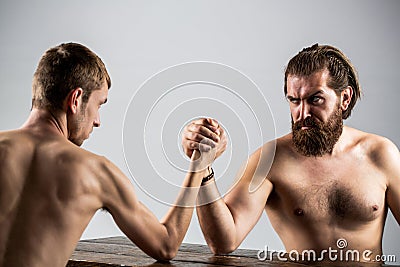 Arm wrestling. Heavily muscled bearded man arm wrestling a puny weak man. Arms wrestling thin hand, big strong arm in Stock Photo