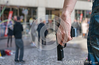 Armed man (attacker) holds pistol in public place. Many people on street. Stock Photo