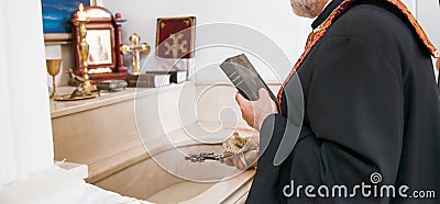 An Armenian priest with a cross and a bible performs the rite of baptism over the font Stock Photo