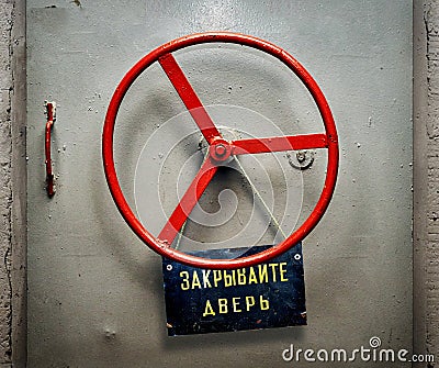 Armored bunker door with hanging shabby signboard with russian CLOSE THE DOOR warning Stock Photo