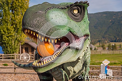 Close-up portrait of Tyrannosaurus Rex statue holding pumpkin in mouth in autumn Editorial Stock Photo