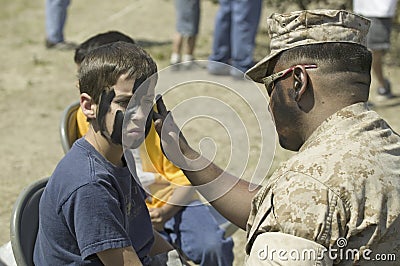 Army solider applying camouflage to young boy Editorial Stock Photo