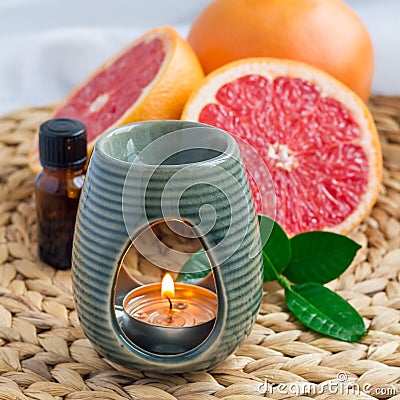 Aroma lamp with grapefruit essential oil on woven mat, grapefruits on background, square format Stock Photo