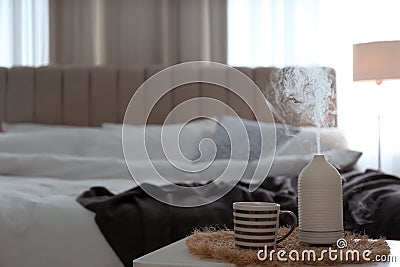 Aroma oil diffuser and cup of tea on table in bedroom. Space for text Stock Photo