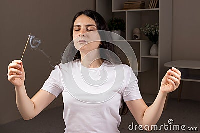 An aromatic Indian stick is burning, the woman in the background is meditating. Aromatherapy, self-immersion, the power Stock Photo