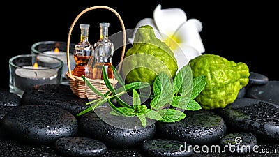 Aromatic spa of bottles essential oil in basket, fresh mint, rosemary, bergamot fruits, flower and candles on black zen stones Stock Photo