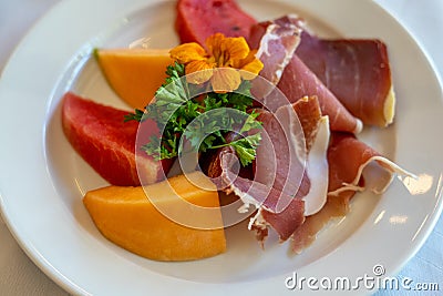 Arrangement of Delicatessen Cold Cuts with charcuterie, melon and watermelon decorated with orange flower and parsley. Soft focus Stock Photo