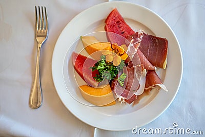 Arrangement of Delicatessen Cold Cuts with charcuterie, melon and watermelon decorated with orange flower and parsley. Soft focus Stock Photo