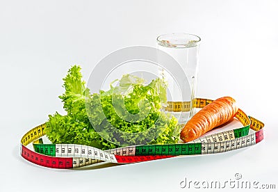 Carrot, green salad leaves and a glass of water surrounded by a measuring tape. Weight loss Stock Photo