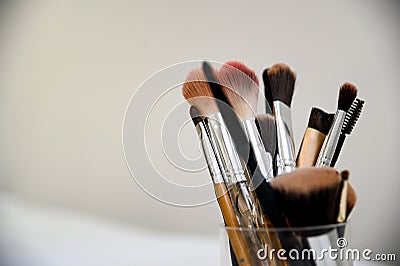 Array of cosmetic makeup brushes arranged in a cup on a wooden tabletop, ready for use Stock Photo