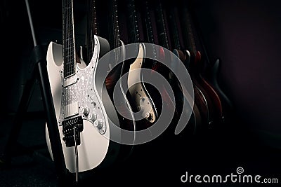 Array of electric guitars are neatly lined up on a rack in the dark Stock Photo