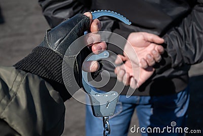 A police officer puts handcuffs on the hands of a bandit Stock Photo