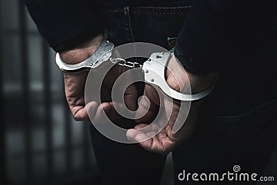 Arrested man with cuffed hands behind prison bars Stock Photo