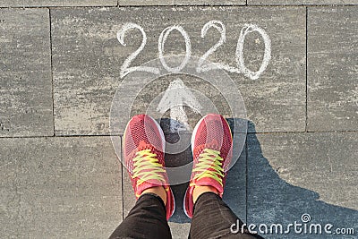2020 arrow forward, written on gray sidewalk with woman legs in sneakers, top view Stock Photo