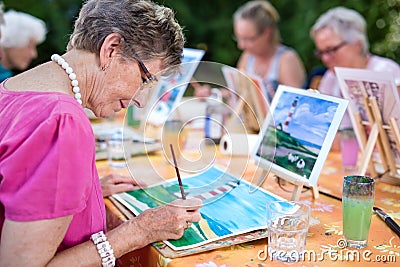 Art therapy for senior ladies, group of women painting the picture of lighthouse from the watercolor template sitting at table. Stock Photo