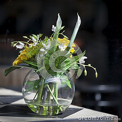 The Artificial bouquet of leaves of monstera Alismatales , gerbera Transvaal daisy and sunflower in the glass vase on the table Stock Photo