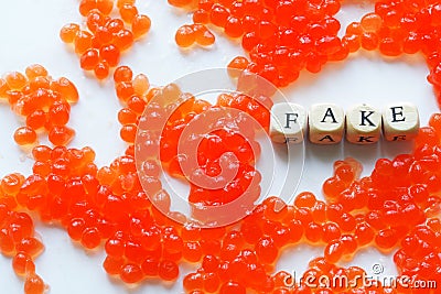 Artificial fake red caviar on a white surface next to the fake sign. The concept of unnatural food, counterfeiting and consumer Stock Photo