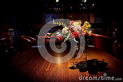 Artificial flowers in a glass bottle are placed on the wooden table with light from the orange lamp, look like the night of a Stock Photo