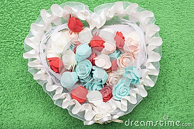 Artificial multicolored roses lie in a white lace basket in the form of a heart Stock Photo