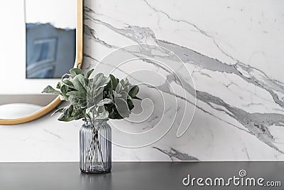 Artificial plant in glass vase compose with gold stainless mirror frame on gray spray-painted working table with marble wall in Stock Photo