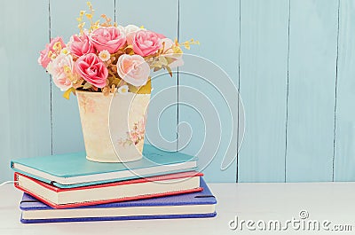 Artificial Rose in flower pot with pile of notebooks Stock Photo