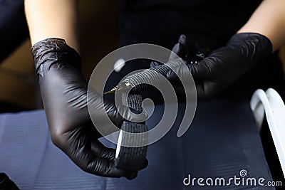 Artist in a black uniform wrap the stretch tape around the tattoo machine for additional fixation Stock Photo