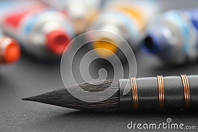 Artistic paintbrush for watercolor painting closeup on black paper sheet of sketchbook. Paint tubes on background Stock Photo