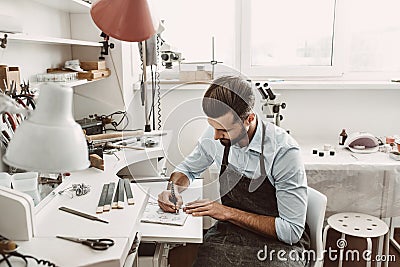 Artistic skills. Young bearded jeweler is drawing a sketch Stock Photo