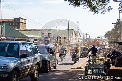 Arusha, Tanzania; 08/06/2019: Lifestyle picture. Cars and motorbikes driving on a road in Arusha with poor buildings on both sides Editorial Stock Photo