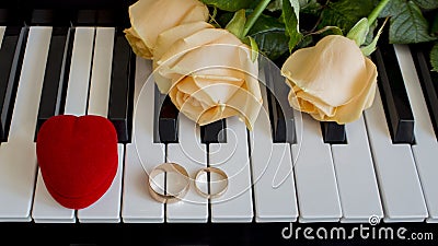 As a gift to the beloved woman, yellow roses lie on the piano with Engagement ring and a red box in the shape of a heart on the Stock Photo