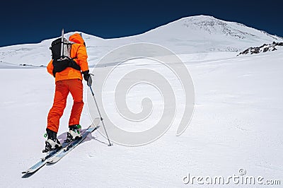 Ascent of a skier with a backpack in a mask and sunglasses on skis with poles to go uphill for freeride and backcountry Stock Photo